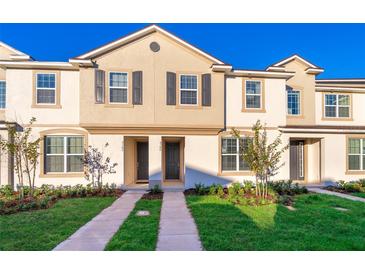 Tan two-story townhome with dark gray shutters and doors, a paved walkway, and well-manicured lawn at 2166 Fleming Mist Pl, Kissimmee, FL 34747