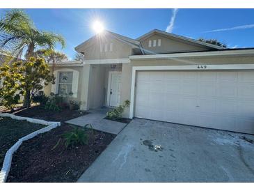 Tan house with a two-car garage and landscaping at 449 Heather Hill Blvd, Davenport, FL 33837