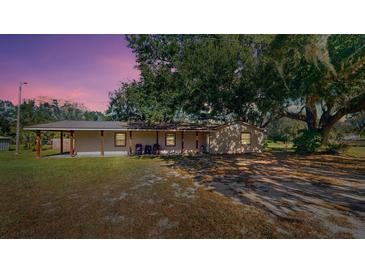 Tan house with covered porch, large tree, and spacious yard at 1335 Dean St, Mulberry, FL 33860