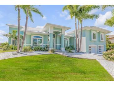 Two-story waterfront home with a light teal exterior, lush landscaping, and a large driveway at 444 Quay Assisi, New Smyrna Beach, FL 32169
