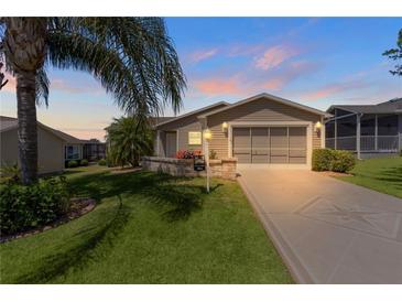 Tan house with a two-car garage, palm trees, and landscaped yard at dusk at 384 Arbella Loop, The Villages, FL 32162