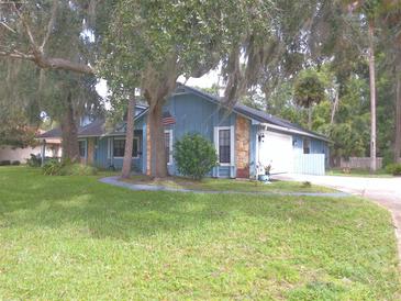 Blue house exterior with stone accents, spacious yard, and mature trees at 573 Pelican Bay Dr, Daytona Beach, FL 32119
