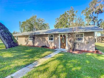 Tan brick ranch home with a brown door and landscaped yard at 2129 Lime Tree Dr, Edgewater, FL 32141
