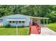 Light teal mobile home with red ramp access and covered carport at 410 Tarrson Blvd, The Villages, FL 32159