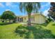 Landscaped backyard with spacious lawn, palm tree, and screened porch at 1213 El Esparza Ln, The Villages, FL 32159