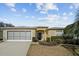 Tan house with a two-car garage, lush landscaping, and a walkway at 15300 Sw 14Th Avenue Rd, Ocala, FL 34473