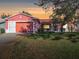 Evening view of a single-story pink house with a two-car garage at 33236 Grand Cypress Way, Leesburg, FL 34748