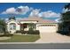 Tan one-story house with a two-car garage and landscaped front yard at 1443 Greenville Way, The Villages, FL 32162