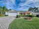 Brick paved driveway leads to a beige house with an orange door and lush landscaping at 941 Eastmont Ct, The Villages, FL 32162