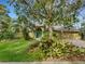 House exterior featuring a teal front door, mature landscaping, and a large tree at 3845 Garnet Dr, Mulberry, FL 33860