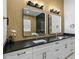 Double vanity bathroom with black countertop, illuminated mirrors, and wood wall at 2728 Sunrise Landing Ln, Lakeland, FL 33812