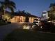 Home's exterior at night, illuminated by landscape lighting, with a driveway and parked vehicles at 561 Meandering Way, Polk City, FL 33868
