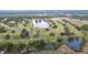 Aerial view of a golf course community with a clubhouse, pond, and lush landscaping at 6029 Avocado Dr, Indian Lake Estates, FL 33855