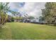 Spacious backyard with green grass, trees, and a light blue house in the background at 835 Heathercrest, Lakeland, FL 33813