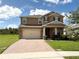 Two story home with tan exterior, paver driveway, and landscaping at 4749 Riverwalk Dr, St Cloud, FL 34771