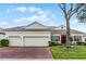 Beige house with three-car garage, red brick driveway, and lush landscaping at 2572 Squaw Crk, Clermont, FL 34711