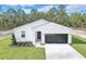 White house with black garage door, landscaping, and a long driveway at 12590 Sw 89Th St, Dunnellon, FL 34432