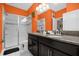 Modern bathroom with a double vanity, walk-in shower, and vibrant orange walls at 1528 Mulligan Blvd, Davenport, FL 33896