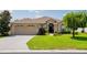 Tan one-story house with a two-car garage, landscaped yard, and brick paver driveway at 15890 Sw 11Th Terrace Rd, Ocala, FL 34473