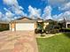 Tan house with white garage doors, landscaped yard, and a patterned driveway at 16376 Sw 13Th Ter, Ocala, FL 34473
