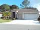 Tan house with a two-car garage and landscaped yard at 9450 Se 130Th Place Rd, Summerfield, FL 34491