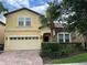 Two-story house with a yellow facade, brick driveway, and lush landscaping at 2131 Tripoli Ct, Kissimmee, FL 34747