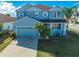 Close-up front view of a two-story blue house with a driveway, garage, and palm trees at 1079 Berkeley Dr, Kissimmee, FL 34744
