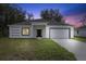 Modern single story home with white exterior, gray roof, and a black front door at dusk at 1312 Congo Dr, Poinciana, FL 34759