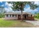 Tan one-story house with a wooden porch and large tree in the front at 1230 8Th Ave, Deland, FL 32724