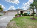 One-story house with beige exterior, two-car garage, and lush landscaping at 1751 Ashwood Run, The Villages, FL 32162