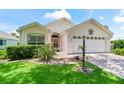 Charming light-colored house with landscaping, a brick driveway and a two-car garage at 1405 W Schwartz Blvd, The Villages, FL 32159