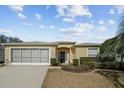 Tan house with a two-car garage, lush landscaping, and a walkway at 15300 Sw 14Th Avenue Rd, Ocala, FL 34473