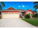 Red house with three-car garage, mature landscaping, and a large driveway at 25611 Maurepas Ln, Leesburg, FL 34748