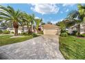 House exterior featuring a brick paver driveway and lush landscaping with palm trees at 877 Winifred Way, The Villages, FL 32162