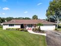 Brick ranch house with brown roof, lush landscaping, and a paved driveway at 1621 Texas Ct, Tavares, FL 32778