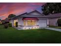 Single-story home with a gray garage door, red awning, and landscaped yard at dusk at 6205 Raven Run, Lakeland, FL 33809