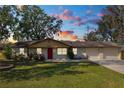 Brick ranch home with red door, two-car garage, and manicured lawn at dusk at 5860 E Starling Dr, Mulberry, FL 33860