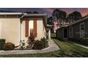 Evening view of tan villa with orange shutters, walkway, and nicely landscaped gardens at 26951 White Plains Way, Leesburg, FL 34748