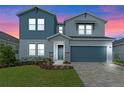 Two-story home with gray and blue siding, stone accents, and a two-car garage at dusk at 1352 Silo Dr, St Cloud, FL 34771