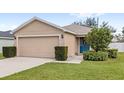 Tan house with a blue front door, two-car garage, and landscaped yard at 4720 Summerfield Cir, Winter Haven, FL 33881