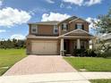 Two story home with tan exterior, paver driveway, and landscaping at 4749 Riverwalk Dr, St Cloud, FL 34771