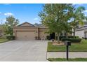 Beige house with a three car garage, manicured lawn, and mature trees at 5307 Cortland Dr, Davenport, FL 33837
