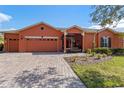Front view of a single-story house with orange exterior, a three-car garage, and a well-maintained lawn at 1221 Glendora N Rd, Kissimmee, FL 34759