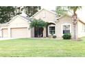 Tan one-story house with three-car garage and manicured lawn at 4420 Heritage Trl, Leesburg, FL 34748