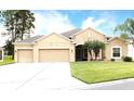 Tan one-story house with three-car garage and manicured lawn at 4420 Heritage Trl, Leesburg, FL 34748