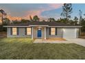 Gray house with blue door, two-car garage, and front yard at dusk at 22043 Sw Rainbow Lakes Blvd, Dunnellon, FL 34431