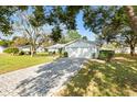 White house with gray roof and a brick paver driveway, surrounded by lush landscaping at 10195 Se 178Th Pl, Summerfield, FL 34491