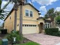 Two-story house with a yellow facade, brick driveway, and lush landscaping at 2131 Tripoli Ct, Kissimmee, FL 34747