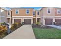 Tan three-story townhouses with brown garages, landscaping, and a paved driveway at 1336 Chelsea Dr, Davenport, FL 33897