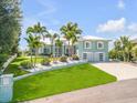 Two-story waterfront home with a light teal exterior, lush landscaping, and a large driveway at 444 Quay Assisi, New Smyrna Beach, FL 32169
